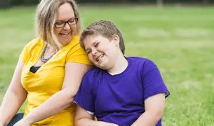 ילד ואמא שלו יושבים יחד עם הדשא וצוחקים יחד