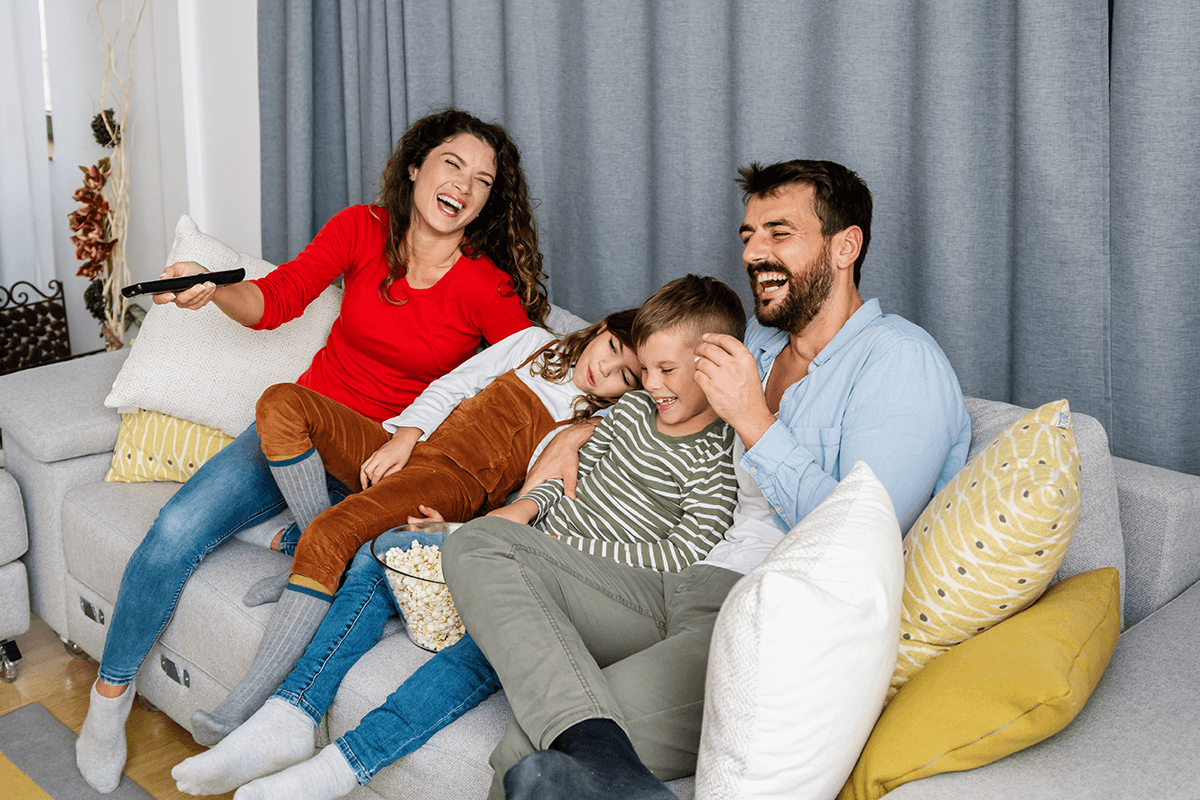 אבא, אמא הבן והבת יושבים על הספה עם פופקורן וצוחקים יחד