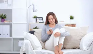 אישה צעירה יושבת על הספה נכנסת בקלות לאפליקציה האמצעות סיסמה חד פעמית