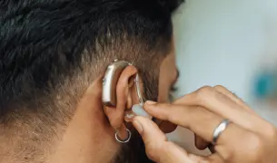 גבר צעיר חרש עם מכשיר שמיעה נהנה משירותי לאומתי המונגשים ללקויי שמיעה