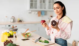 בחורה מתלבטת במה לבחור- בתפוח או סופגניה