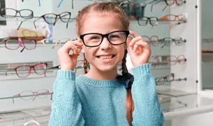 ילדה קטנה מודדת ומתנסה בזוגות של משקפיים באחת מחנויות האופרטיקה שבהסדר עם לאומית