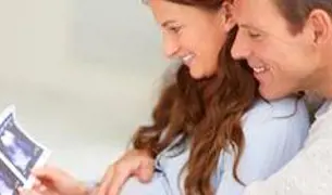 זוג יושבים מחובקים ומתבוננים בתמונות אולטרסאונד של תינוק