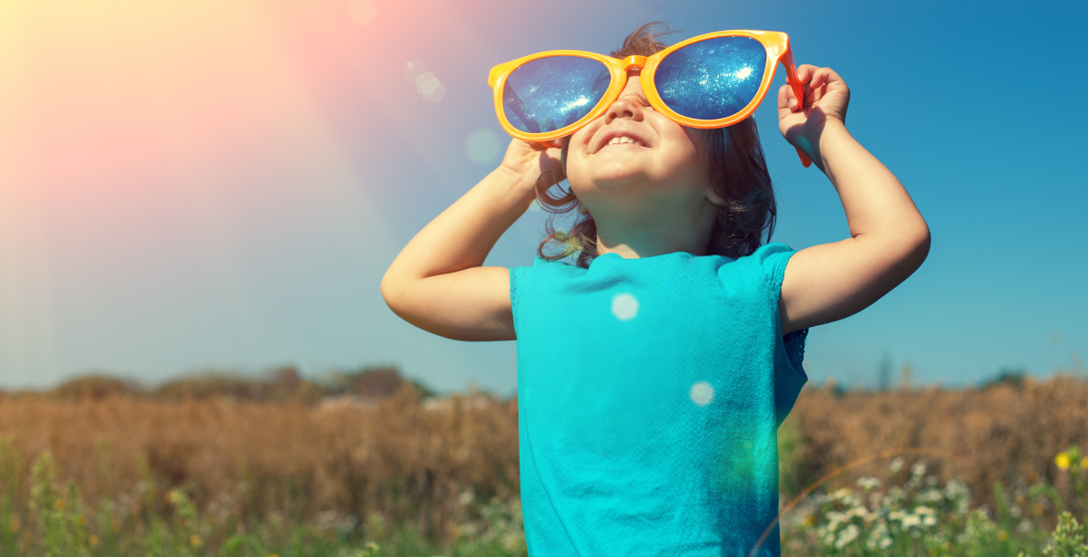 ילד קטן בתוך שדה פרחים מתבונן למעלה על משקפי שמש מאד גדולים על העיניים 