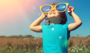ילד קטן בתוך שדה פרחים מתבונן למעלה על משקפי שמש מאד גדולים על העיניים 