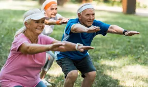 שתי נשים וגבר, כולם קשישים, עושים סקוואטים על הדשא