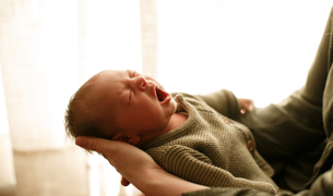 תינוקת קטקנה בת חודש מפהקת בידיים של אמא שלה