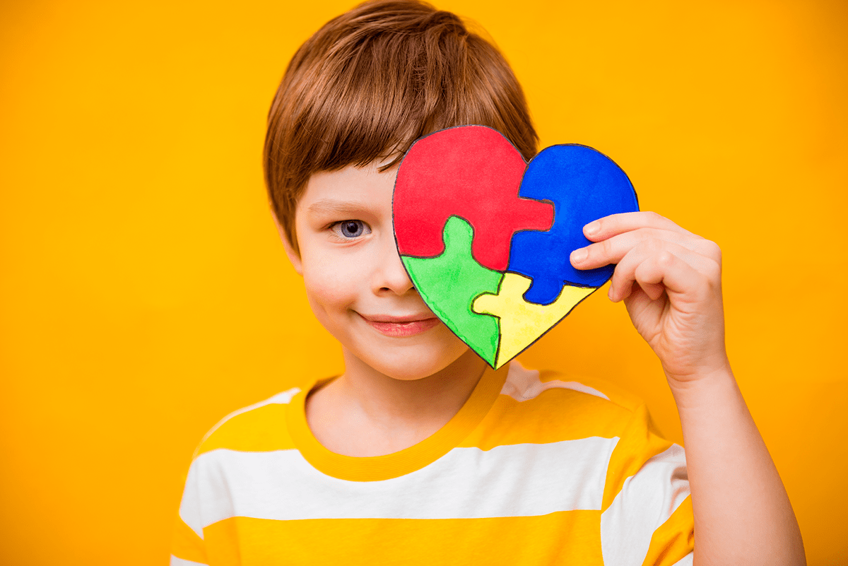 ילד קטן מחזיק לב בצבעים של מודעות לאוטיזם