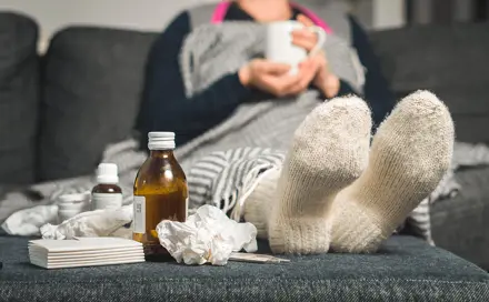 A woman who is not feeling well is holding a glass and next to the woman is medicine