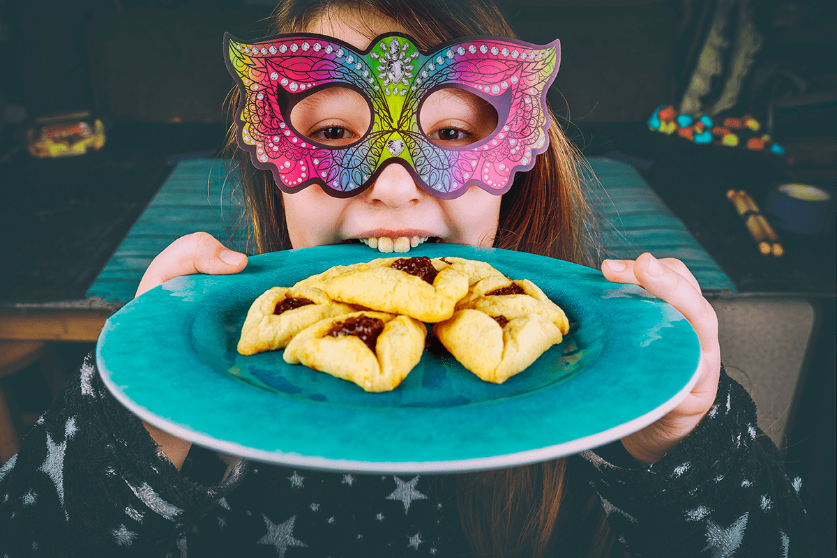 ילדה עם מסיכה מחזיקה צלחת עם אוזני המן 