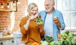 זוג מבוגרים עומדים במטבח עם הרבה פירות ויורות וצוחקים