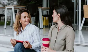שתי נשים בכיל המעבר יושבות מחוץ למשרד עם קפה ומדברות