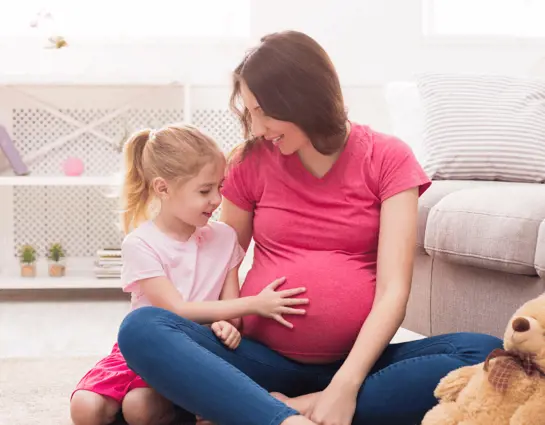 אמא הריונית משחקת על הרצפה עם הבת הקטנה שלה 