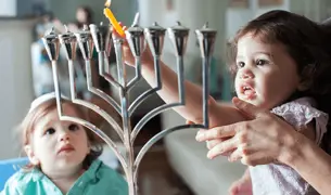 ילדה מדליקה נר חנוכה עם ליווי אחד ההורים