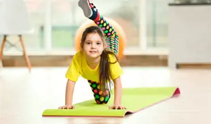 ילדה קטנה עם חולצה צהובה עושה ספורט בבית