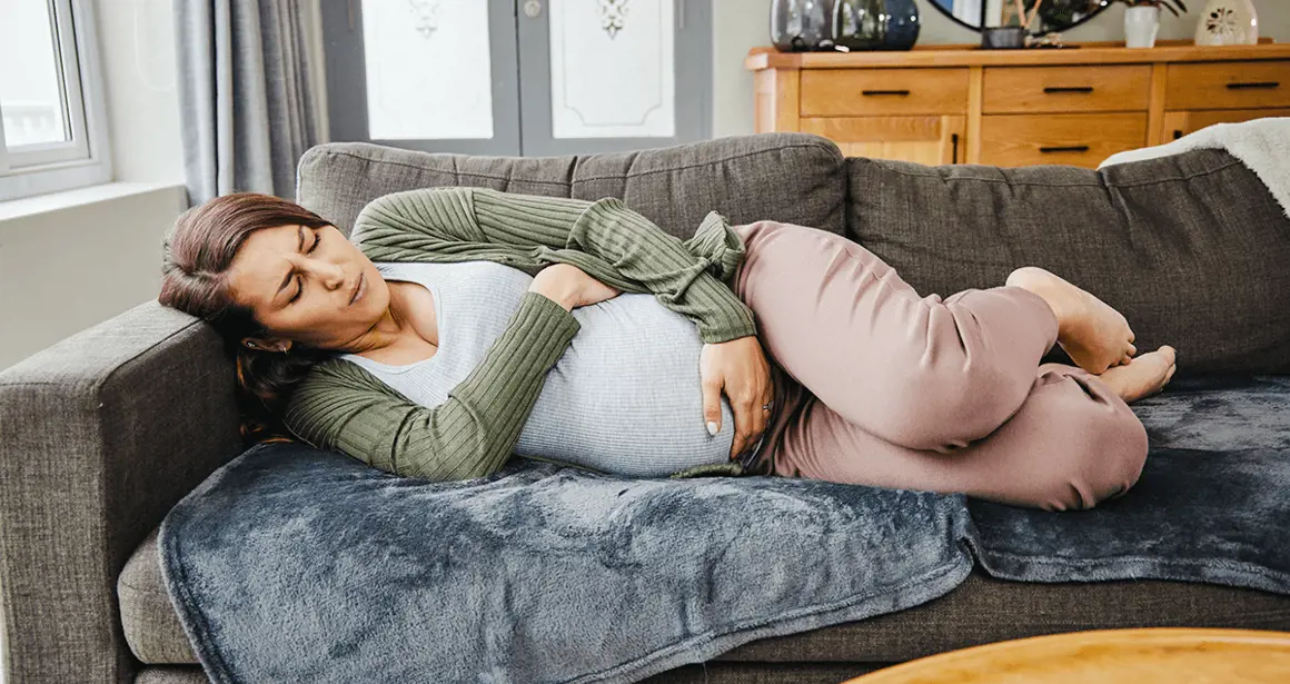 A woman holds her stomach and lies on the sofa