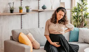 אישה בהריון יושבת בספה, כואב לה הגב