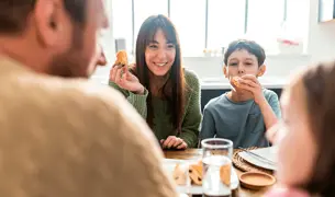 אמא, אבא, ילד וילדה יושבים סביב שולחן ואוכלים