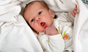 תינוקת בת 3 חודשים, שוכבת עטפוה בשמיכה עם פה פתוח