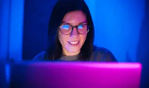 אישה מרכיבה משקפיים נגד אור כחול ומסתכלת במחשב