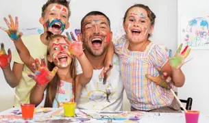 אבא ושלושה ילדים מאד שמחים צובעים בצבעי ידיים ועושים בלאגן