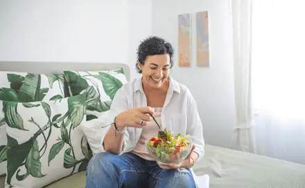 אישה יושבת על המיטה ומחזיקה קערה עם סלט