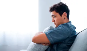 A boy sits on the sofa, hugs a pillow and thinks