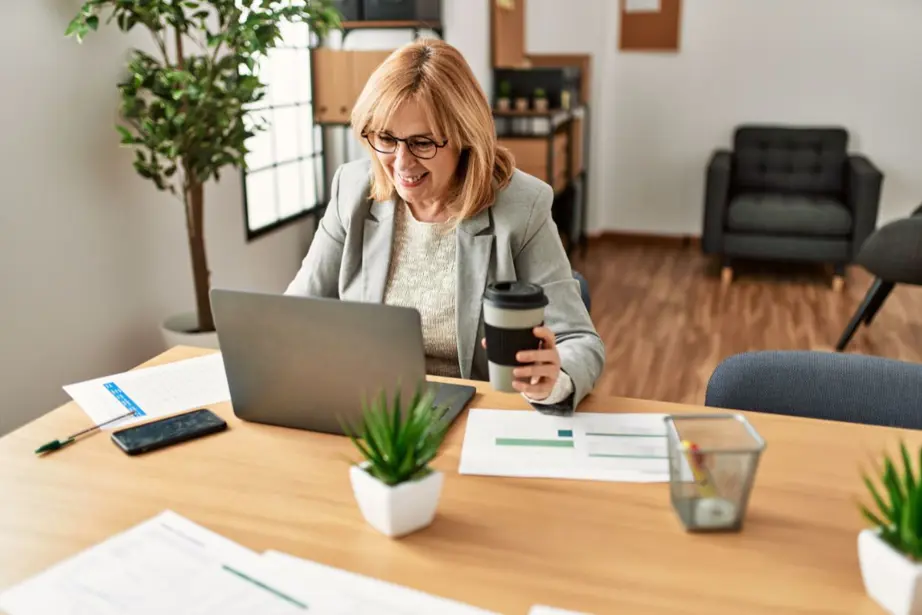 אישה בגיל המעבר יושבת מול מחשב עם כוס קפה