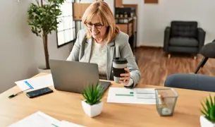 אישה בגיל המעבר יושבת מול מחשב עם כוס קפה