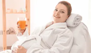 אישה הריונית יושבת עם חלוק ושותה מיץ כשהיא ממתינה לטיפול רפואה משלימה
