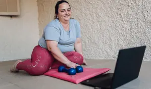 אישה יושבת מול מחשב עם משקולות ועושה ספורט